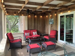 Eine überdachte Terrasse mit Korbmöbeln, roten Kissen und Lichterketten.