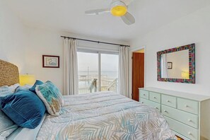 A bedroom with a bed, a ceiling fan, a window with curtains, a dresser, and a mirror. - The Purple Beach House (Rockport)