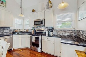 A kitchen with white cabinets, a stainless steel oven, a microwave, and a black countertop. - The Purple Beach House (Rockport)