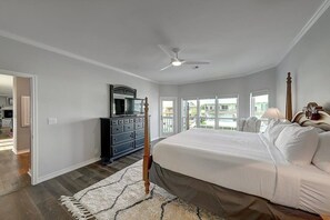 Quarto com cama grande, penteadeira, ventilador de teto e vista para o exterior.