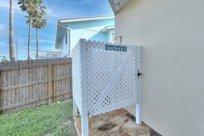A white wooden fence with a 'Shower' sign, a stone-paved area, and a light blue building in the background. - Curlew Casa - Waterfront, Pool & Dogs OK (Rockport)