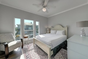 A bedroom with a bed, a chair, a bedside table, a lamp, and a window with a view of a house. - Curlew Casa - Waterfront, Pool & Dogs OK (Rockport)