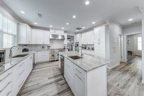 A modern kitchen with white cabinetry, a marble countertop island, and a wood floor. - Inkies Retreat - Waterfront Home with Swim Spa (Rockport)