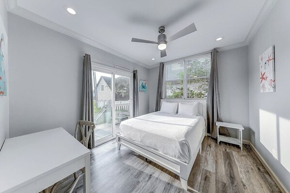 A bedroom with a bed, a desk, a ceiling fan, and a view through a sliding glass door. - Inkies Retreat - Waterfront Home with Swim Spa (Rockport)