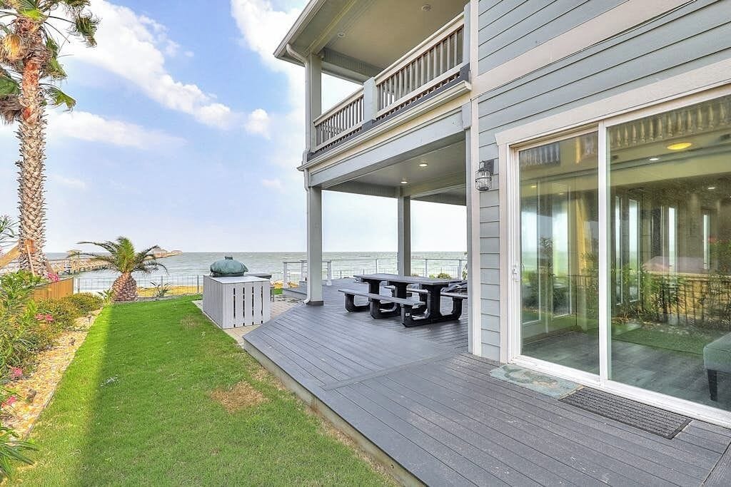 A two-story house with a covered patio, a view of the ocean, and outdoor furniture.
