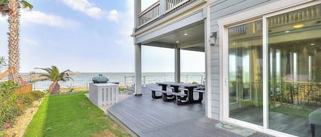 A two-story house with a covered patio, a view of the ocean, and outdoor furniture.