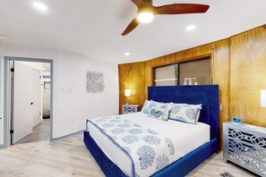 A bedroom with a bed, wooden paneling, a ceiling fan, and a nightstand. - Cupola del Mare - Gulf Views, Fireplace & Loft (Galveston)