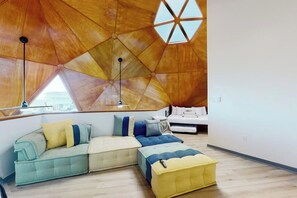 A modern interior with a geometric wooden ceiling, a sectional sofa, a small ottoman, and a white bed. - Cupola del Mare - Gulf Views, Fireplace & Loft (Galveston)