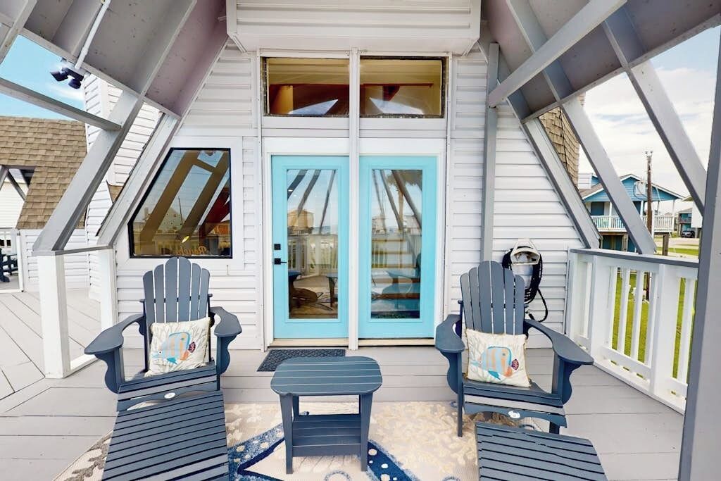 Un porche abrité avec deux fauteuils Adirondack, une petite table et une porte bleue dotée de panneaux de verre.