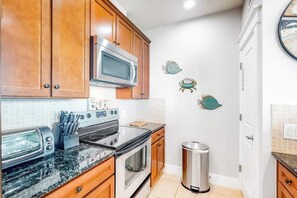 A kitchen with wooden cabinets, a microwave, a toaster, and a trash can. - Pointe West Resort - Peaceful at the Pointe (Galveston)