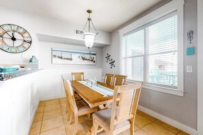 A dining area with a wooden table and chairs, a large wall clock, and artwork. - Pointe West Resort - Peaceful at the Pointe (Galveston)