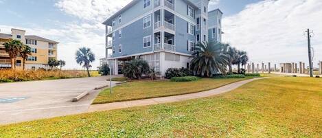 A multi-story residential building with a flat roof, balconies, and a landscaped lawn.