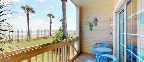 A balcony with a wooden railing, two blue chairs, and a view of the beach with palm trees.