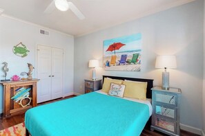 A bedroom with a bed, nightstands, a painting, and a door. - Dawn Condominiums - The Perfect Dawn (Galveston)