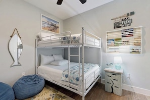 Une chambre avec un lit superposé, une échelle, une petite table de chevet avec une lampe, un miroir et une étagère avec des livres et des objets décoratifs.