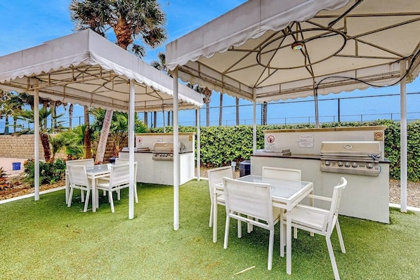 Une terrasse extérieure avec un barbecue, des tables et des chaises blanches.