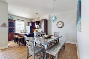 A dining area with a wooden table and chairs, a kitchen in the background, and a clock on the wall. - Infinity Sea of Serenity (Galveston)