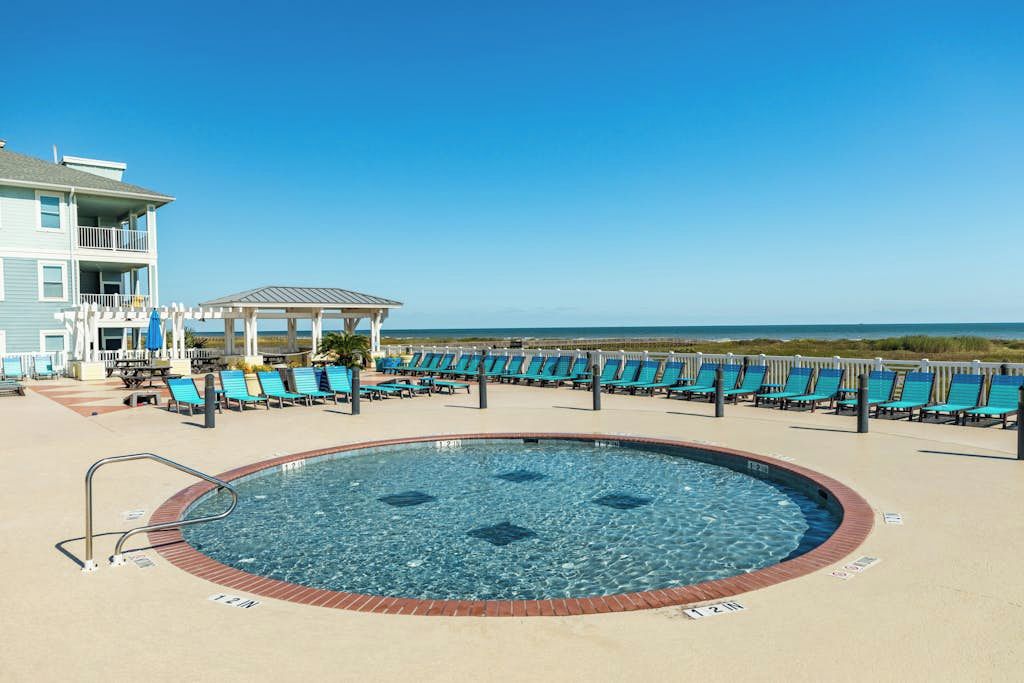 A pool area with a circular pool, lounge chairs, and a building with a balcony.
