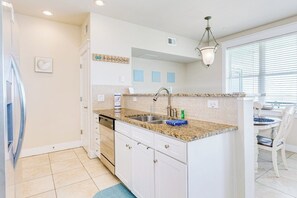 A kitchen with white cabinets, a granite countertop, a built-in dishwasher, and a hanging light fixture. - Pointe West Resort - OceanScape (Galveston)