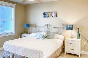 A bedroom with a bed, bedside tables, a window with blinds, and a wall-mounted artwork. - Pointe West Resort - OceanScape (Galveston)