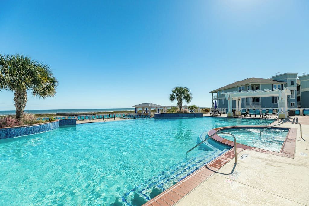 A swimming pool with clear blue water, surrounded by lounge chairs and a building with a balcony.