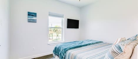 A bedroom with a bed, a ceiling fan, a window, and a wall-mounted TV.