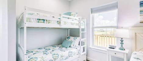 Quarto com beliche, uma mesa pequena com luminária e vista para o exterior.