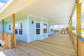 A covered porch with a wooden deck, light blue walls, and a view of the outdoors. - Vacationers Valhalla (Galveston)