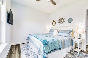 Un dormitorio con cama, mesita de noche, televisor montado en la pared y decoración de temática náutica.