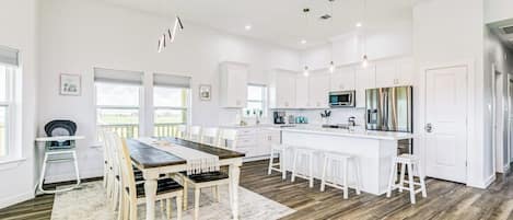 A modern kitchen with white cabinetry, a wooden dining table, and bar stools.