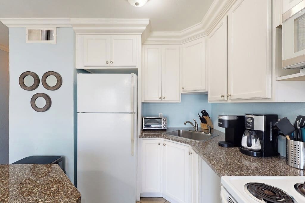 A kitchen with white cabinets, a refrigerator, a toaster, a coffee maker, and a stove.