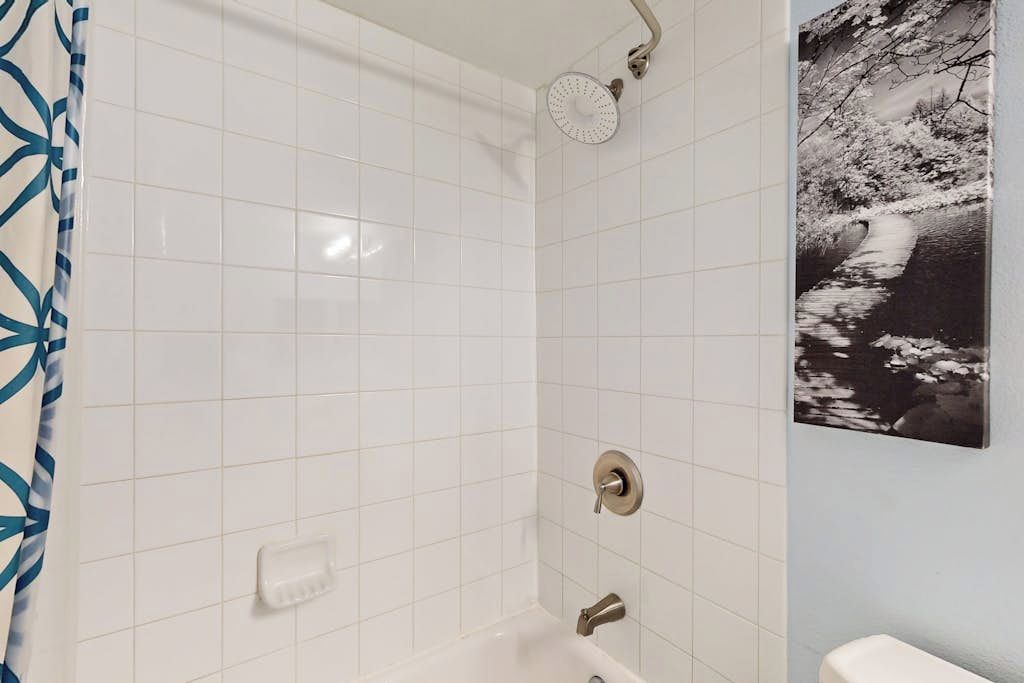Ein Badezimmer mit weißen Fliesen, einer Dusche, einer Toilette und einem gerahmten Bild an der Wand.