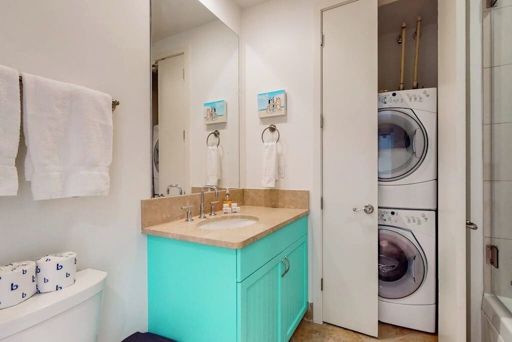 A bathroom with a sink, toilet, and stacked washing machines.