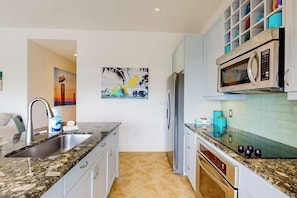 A kitchen with granite countertops, a stainless steel sink, a microwave, and a refrigerator. - Pelican Oasis - Beachfront Condo, Pool & Hot Tub (Galveston)