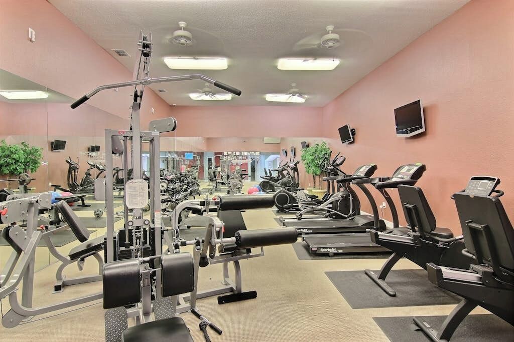 A gym with various exercise equipment, including treadmills and weight machines, and a mirror on the wall.