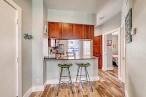 A kitchen with wooden cabinets, a countertop, and two green bar stools. - Beach Club 155 - Pool & Hot Tub, Close to Beach (Corpus Christi)