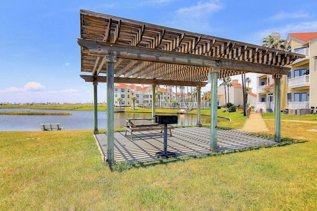 Un área de estar al aire libre techada con una pérgola de madera, un banco y un cubo de basura.