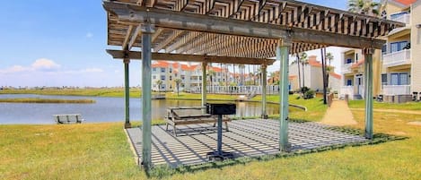 Un área de estar al aire libre techada con una pérgola de madera, un banco y un cubo de basura.