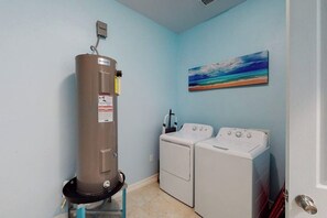 A laundry room with a heater, two washing machines, and a painting on the wall. - Blue Dolphin Beach House (South Padre Island)