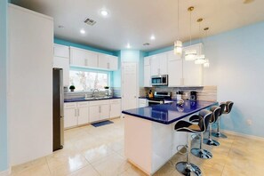 A modern kitchen with white cabinets, a central island with bar stools, and pendant lighting. - Blue Dolphin Beach House (South Padre Island)