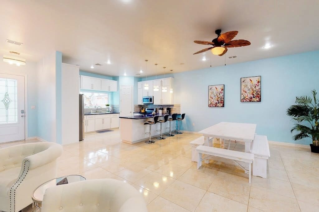 A modern kitchen with white cabinets, a central island with bar stools, and a ceiling fan.