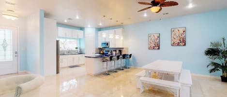 A modern kitchen with white cabinets, a central island with bar stools, and a ceiling fan.