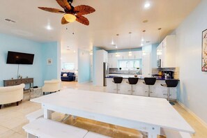 A modern kitchen with a central island, bar stools, and a ceiling fan. - Blue Dolphin Beach House (South Padre Island)