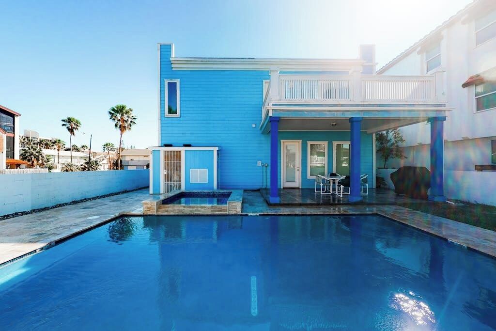 A residential property with a swimming pool, a covered patio, and a two-story building with a blue exterior.