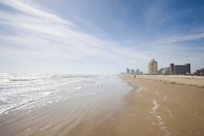 A beach with a clear sky, waves, and buildings in the distance. - Marlin Street C - Pool, 2 Minutes from the Beach (South Padre Island)