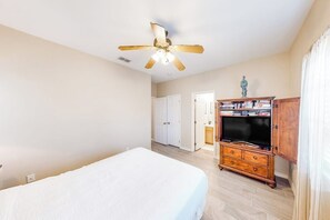 A bedroom with a bed, a wooden dresser, a ceiling fan, and a door leading to another room. - Marlin Street C - Pool, 2 Minutes from the Beach (South Padre Island)