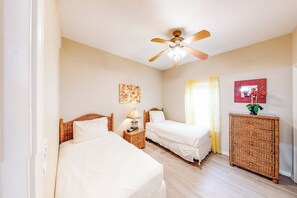 A bedroom with two beds, a ceiling fan, a bedside table with a lamp, and a wicker side table. - Marlin Street C - Pool, 2 Minutes from the Beach (South Padre Island)