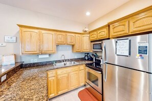 A kitchen with wooden cabinets, granite countertops, stainless steel appliances, and a refrigerator with a note attached. - Marlin Street C - Pool, 2 Minutes from the Beach (South Padre Island)