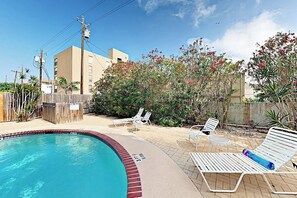 A swimming pool with lounge chairs and a wooden fence. - Marlin Street C - Pool, 2 Minutes from the Beach (South Padre Island)