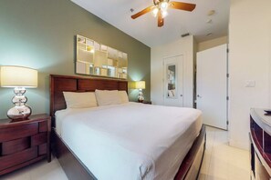 A bedroom with a bed, nightstands, a ceiling fan, a mirror, and a door. - La Isla Condominiums #C105 (South Padre Island)